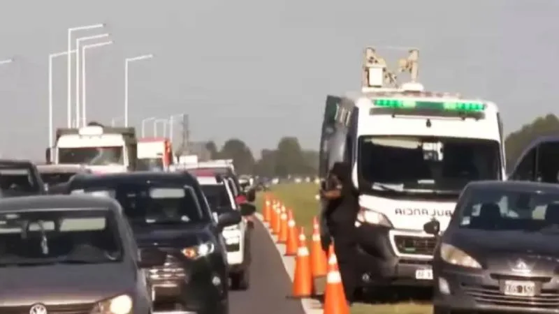 Autopista Rosario-Buenos Aires con tránsito vehicular y cartel de advertencia por baches
