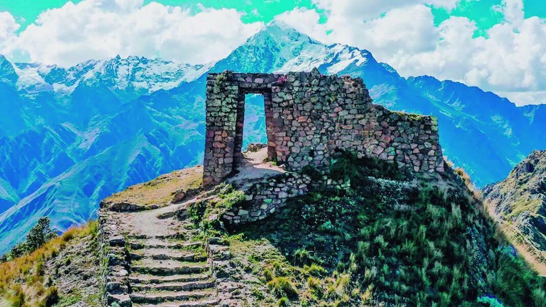 Grupo de caminantes recorriendo un sendero de montaña en los Andes, con vistas a ruinas incaicas.