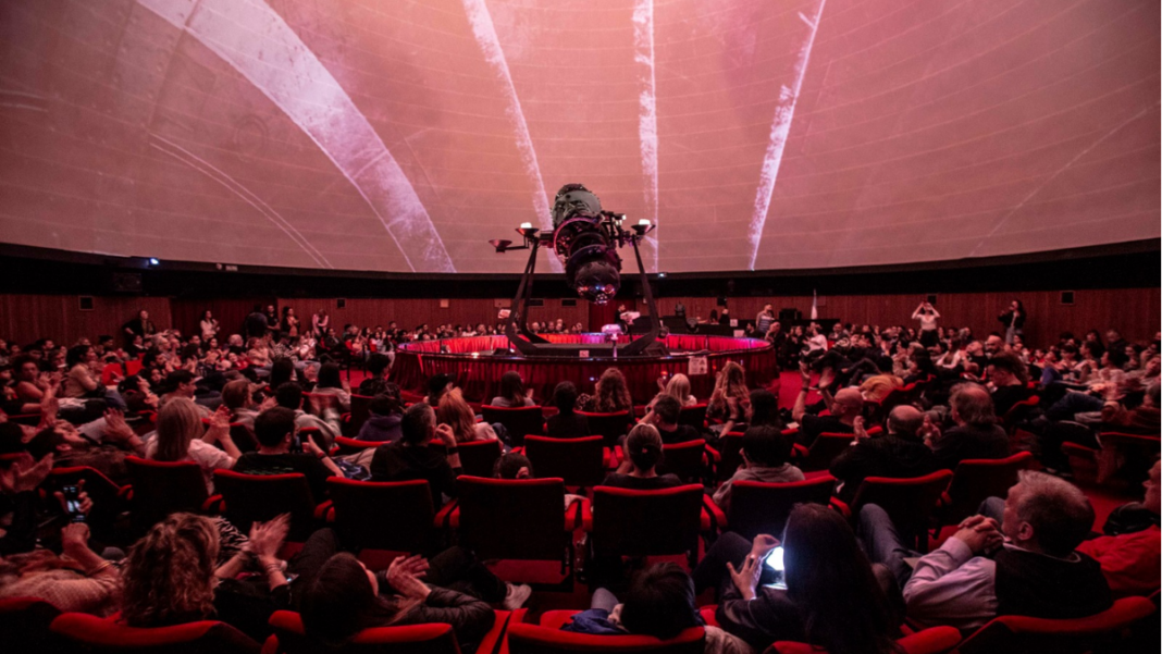 Público dentro de la cúpula del Planetario de Rosario durante una proyección inmersiva, con luces y colores.