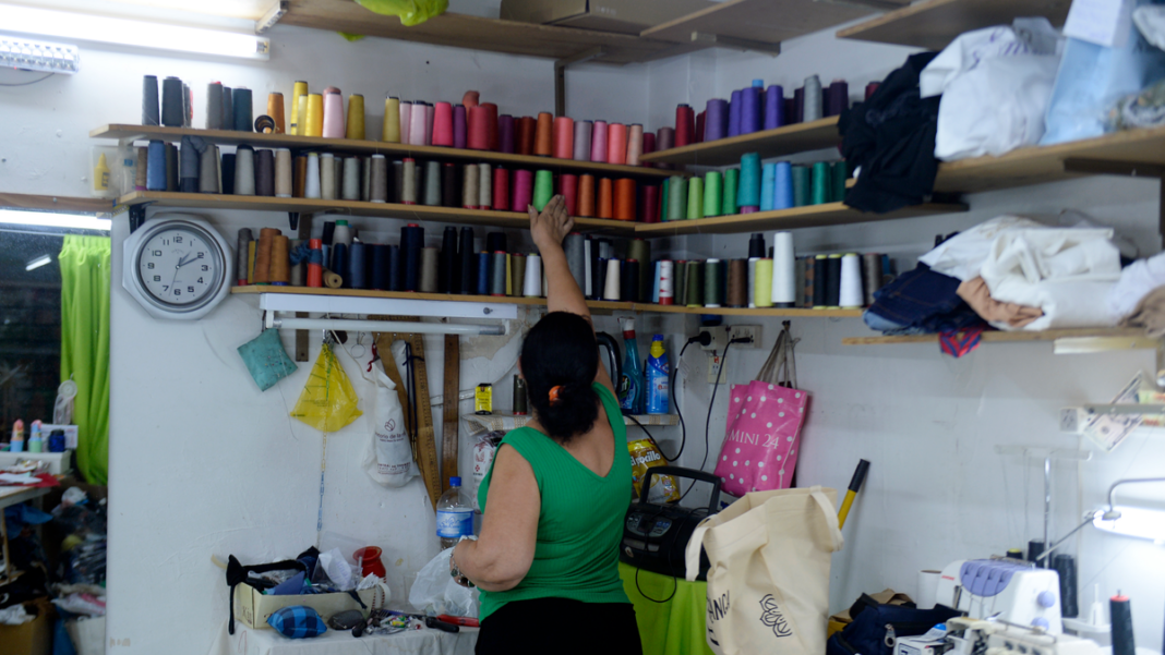 Mujer cosiendo en un taller de arreglos de ropa en Rosario, con prendas colgadas